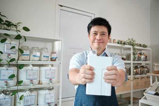 Portrait of Thai male shopkeeper smiles and looks at camera with reusable container, organic products at refill store, zero-waste grocery, and plastic-free, environment-friendly sustainable business. photo