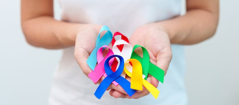 World cancer day, February 4. Hand holding blue, red, green, white, pink, navy blue and yellow ribbons for supporting people living and illness. Healthcare and Autism awareness day concept photo
