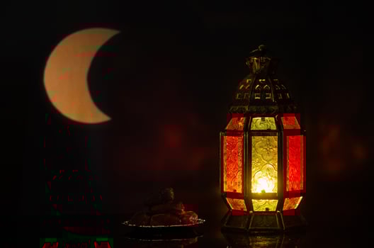 Lantern and small plate of dates fruit with moon shape from light on background for the Muslim feast of the holy month of Ramadan Kareem. photo