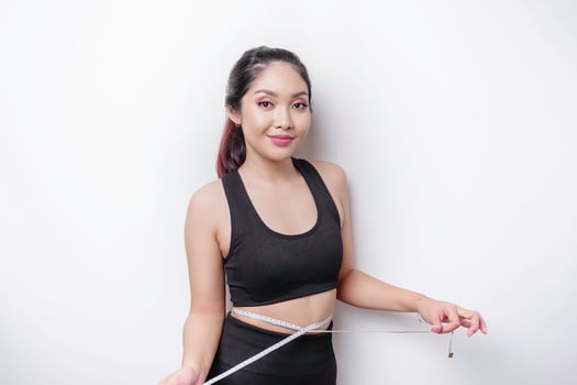 Portrait of cheerful young Asian woman in sportswear measuring waist with tape, feeling happy about losing weight at home. Healthy lifestyle, sports and slimming diet concept photo