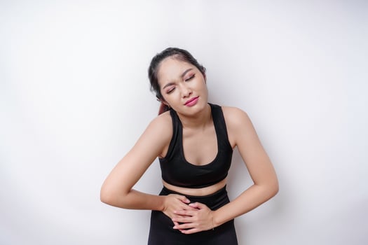 A young unwell sick ill woman wearing sportswear hold hand on stomach suffers pain isolated on white background photo