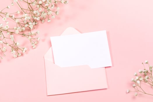 Pastel pink festive layout with envelope, empty sheet, white gypsophila flowers. Copy space for text. Mock up. photo