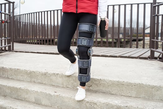 Woman wearing knee brace or orthosis after leg surgery, walking in the park photo