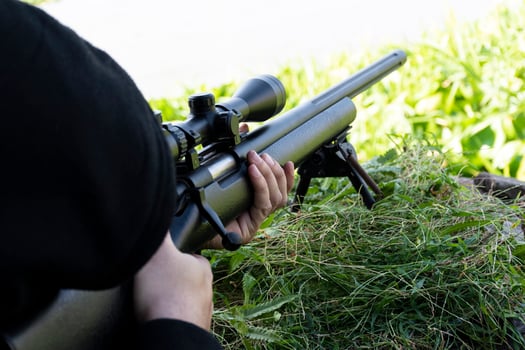 Top view man wearing black hood is shooting rifle looking through scope photo