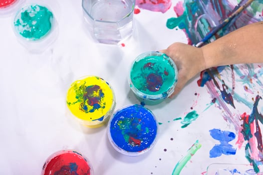 The child holds a jar of watercolor paint in his hand against the background of his drawings. Kids creativity. photo