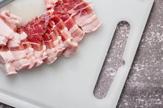 streaky pork is sliced on a white chopping board in the kitchen.Close up cutting slide pork belly raw photo