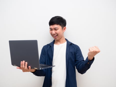 Asian man look at laptop in hand and feel happy show fist up happy smile on white isolated photo