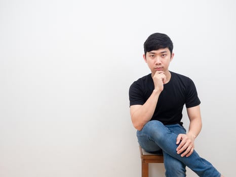 Asian man sitting on chair with confident face looking at camera on white background photo