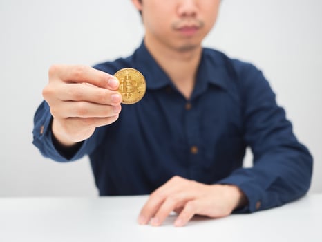 Man sitting at the desk and showing gold bitcoin in his hand photo