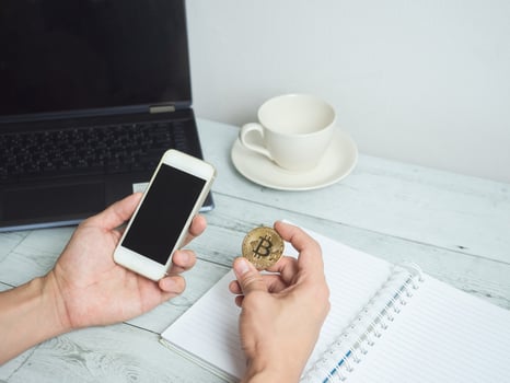 Hand holding gold bitcoin and mobilephone with workspace on white wood table background photo