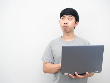 Asian man using laptop and feeling bored looking at copy space photo