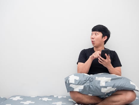 Man using mobile on the bed feeling excited looking at copy space photo