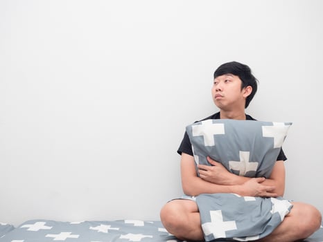 Sleepy man hug pillow on the bed looking at copy space photo