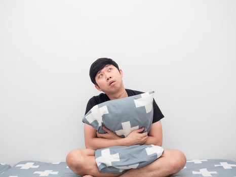 Man hug pillow on the bed looking up at copy space photo