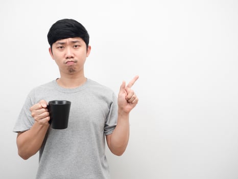 Asian man holding coffee cup unhappy emotion point finger at copy space photo