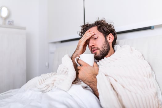 Sick day at home. Handsome Man has fever and common cold. Cough. Closeup Of Young Man Caught Cold Or Flu Illness. Portrait Of Unhealthy man Feeling Pain In Throat and drinking hot beverage. photo
