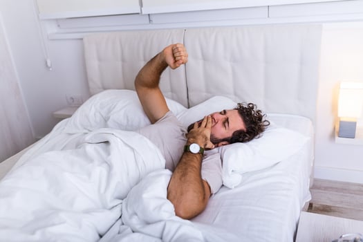 Young man stretching while waking up in the morning. Man yawning while waking up. Lazy young man in sleep. Portrait of man yawns and stretches in bed. photo