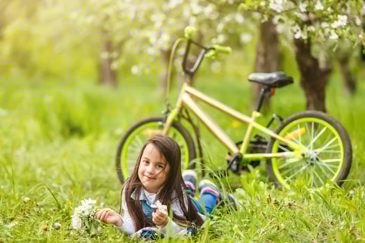 little girl with bike near flowering trees in spring photo