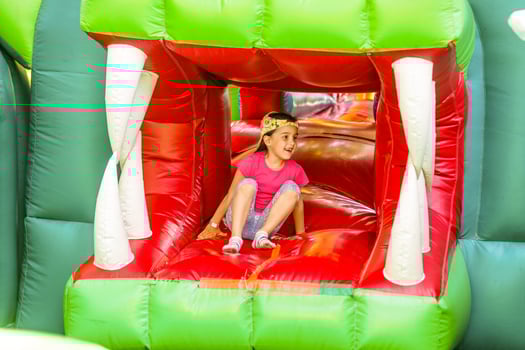 Cute funny preschool little girl in a colorful, jumping and bouncing in an inflatable castle having fun at a children birthday party on a kids playground in summer photo