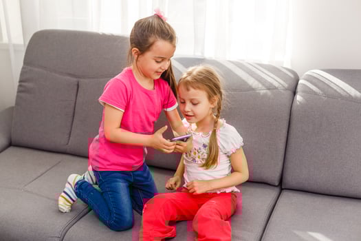 people, children, technology, friends and friendship concept - happy little girls sitting on sofa and taking selfie with smartphone at home. photo