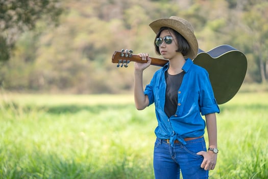 Woman wear hat and carry her guitar in grass field photo