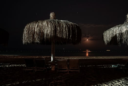 Loungers and thatched parasols arranged on sandy beach at night photo