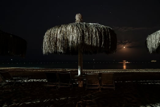 Empty deck chairs and thatched parasols arranged on sandy beach at night photo