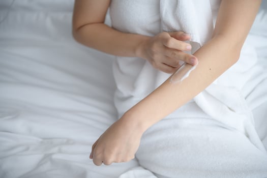 Asia woman sitting on bed and applying cream on body. photo
