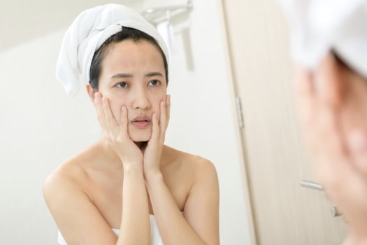 Problem skin. Concerned young asian women popping pimple on cheek while standing near mirror in bathroom. young asian women with acne photo