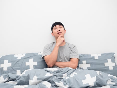 Asian man sitting on the bed gesture thinking about something looking up photo