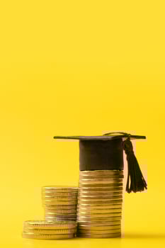 Graduated cap with coins on yellow background. Savings for education concept photo