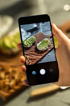 Hands take pictures on smartphone of two beautiful healthy sour cream and avocado sandwiches lying on board on the table. Social media and food concept photo