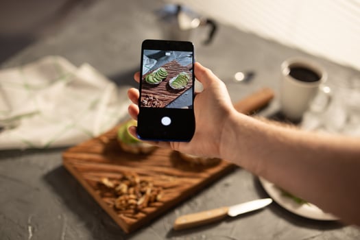 Hands take pictures on smartphone of two beautiful healthy sour cream and avocado sandwiches lying on board on the table. Social media and food concept photo