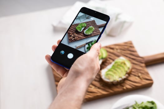 Hands take pictures on smartphone of two beautiful healthy sour cream and avocado sandwiches lying on board on the table. Social media and food concept photo