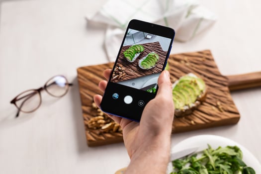 Hands take pictures on smartphone of two beautiful healthy sour cream and avocado sandwiches lying on board on the table. Social media and food concept photo