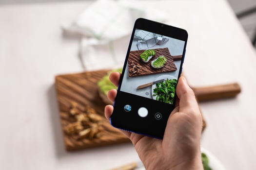 Hands take pictures on smartphone of two beautiful healthy sour cream and avocado sandwiches lying on board on the table. Social media and food concept photo