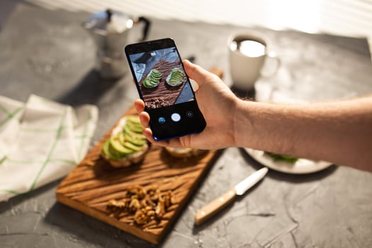 Hands take pictures on smartphone of two beautiful healthy sour cream and avocado sandwiches lying on board on the table. Social media and food concept photo