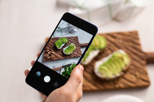 Hands take pictures on smartphone of two beautiful healthy sour cream and avocado sandwiches lying on board on the table. Social media and food concept photo