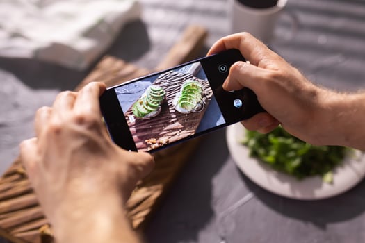 Hands take pictures on smartphone of two beautiful healthy sour cream and avocado sandwiches lying on board on the table. Social media and food concept photo