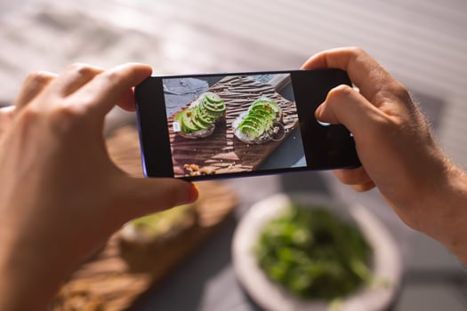 Hands take pictures on smartphone of two beautiful healthy sour cream and avocado sandwiches lying on board on the table. Social media and food concept photo