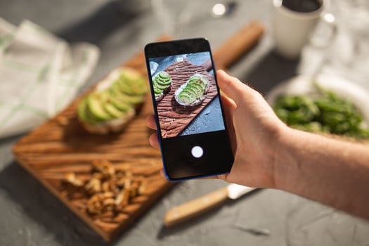 Hands take pictures on smartphone of two beautiful healthy sour cream and avocado sandwiches lying on board on the table. Social media and food concept photo