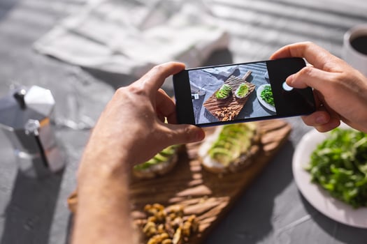 Hands take pictures on smartphone of two beautiful healthy sour cream and avocado sandwiches lying on board on the table. Social media and food concept photo