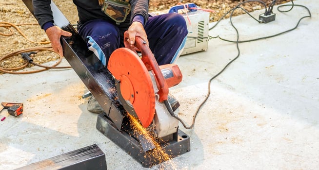 The worker in the work clothes uses an electric steel cutter. Cutting large steel bars at the construction site photo
