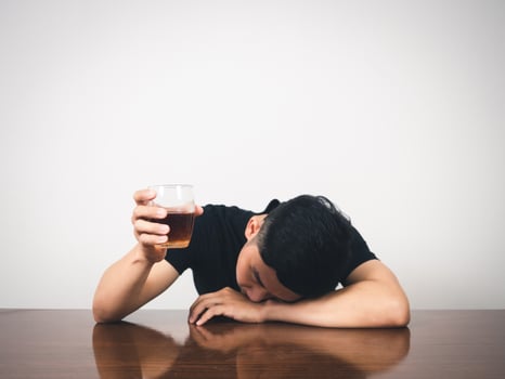 Man alcoholism hangover laying at table and hold alcohol glass in hand photo