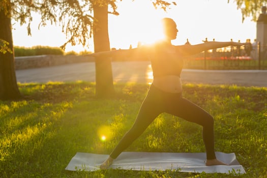 Cute young pregnant woman in black tracksuit makes heroe pose standing barefoot on rug on green lawn on sunny summer day. Childbirth preparation and nervous calming concept photo