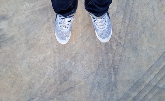 Top view of leg wearing blue jeans and gray or grey sneakers or fashion shoes on floor with car wheel or brake mark on road or street with copy space. Flat lay of part body. Abstract background photo