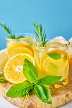 Glass of water with orange, mint and rosemary on blue background photo