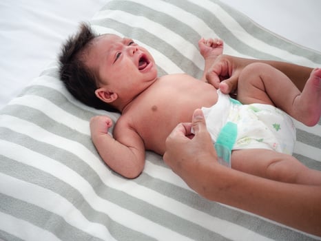 Cute baby girl crying while her mother changed her diaper. Mixed-race Asian-Australian infant dress up after bathing by her mommy. Health care concept. photo