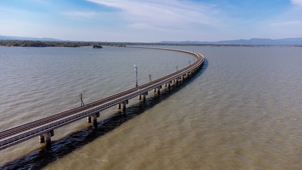 Aerial view of an amazing travel train parked on a floating railway bridge over the water of the lake in Pa Sak Jolasid dam with blue sky at Lopburi, Thailand. photo