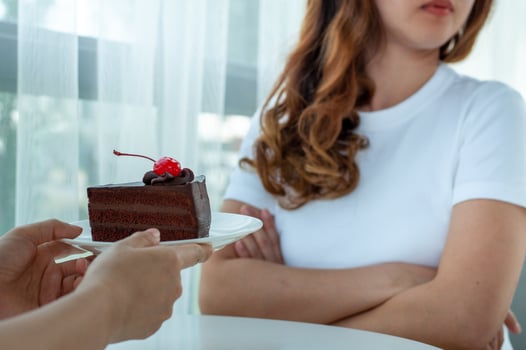 Hands handing a plate on a chocolate cake to a young woman dieting But she refuses to eat. photo